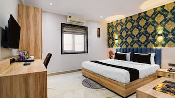 A modern hotel room with a bed, bedside table, desk, chair, and a television.