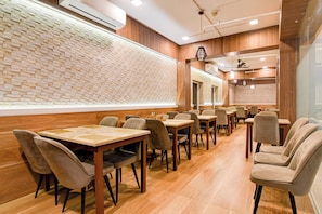 A restaurant interior with brick-patterned walls, wooden flooring, and a series of tables and chairs. - Palette Dumdum Airport Formerly Seventy (Kolkata)