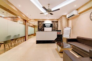 Zona de recepción de un hotel, con un mostrador, un área de espera con sofá y un ventilador de techo.