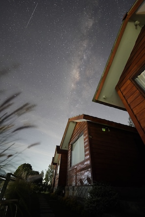 Cielo nocturno con estrellas, una casa de madera con ventana, y una vista despejada del cielo.