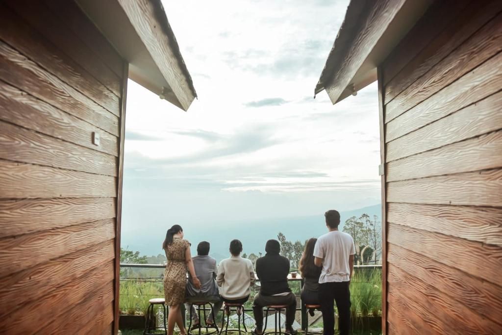 A group of people seated on stools facing a scenic outdoor view through wooden-framed windows.