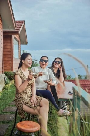 Tres personas sentadas en una mesa al aire libre, con vista a un edificio de madera y vegetación.