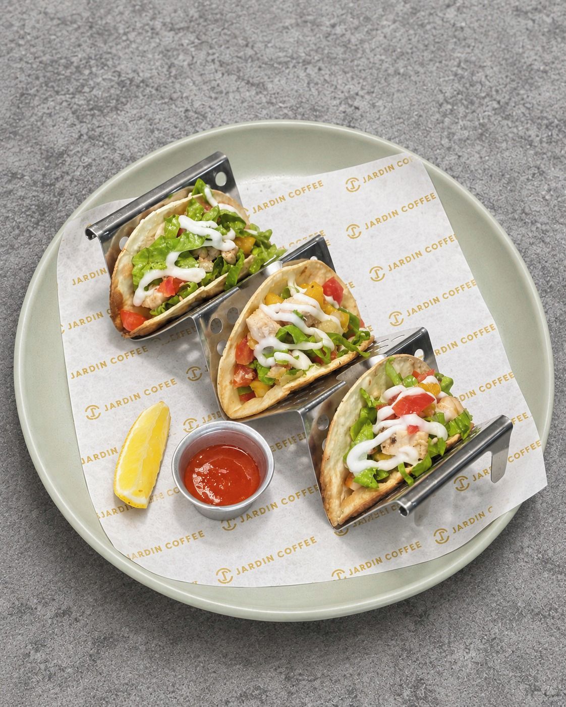 Three tacos on a plate with a lemon wedge and a small bowl of sauce.