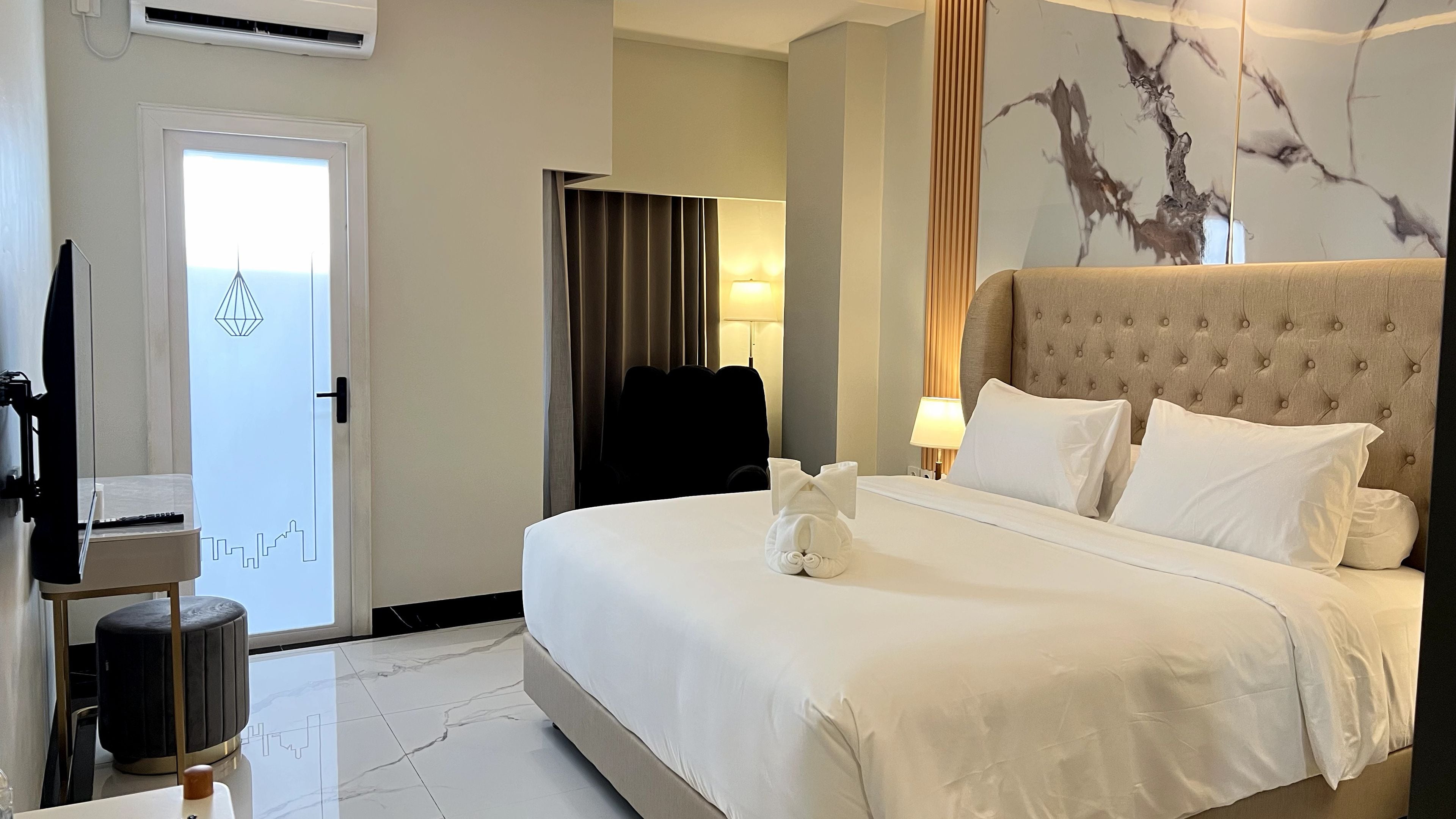 A hotel room with a bed, a flat-screen TV, a lamp, and a wall-mounted air conditioner.