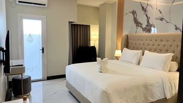 A hotel room with a bed, a flat-screen TV, a lamp, and a wall-mounted air conditioner.