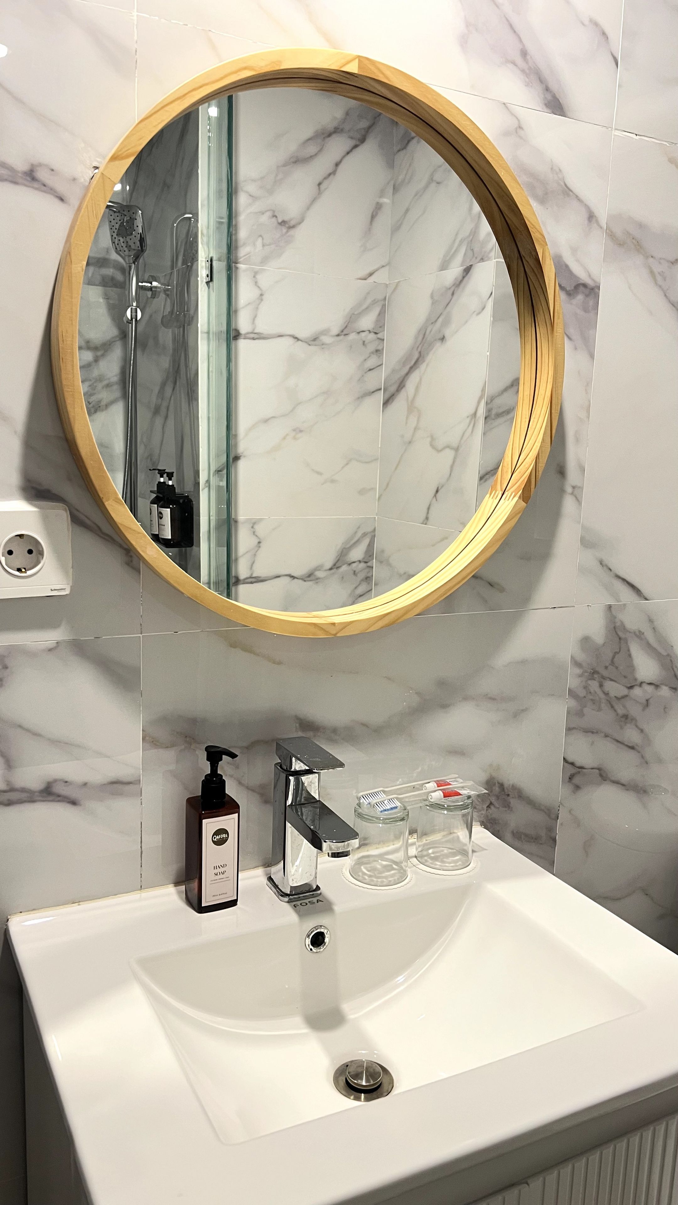 Une salle de bain avec un miroir rond, un lavabo et une douchette à main.
