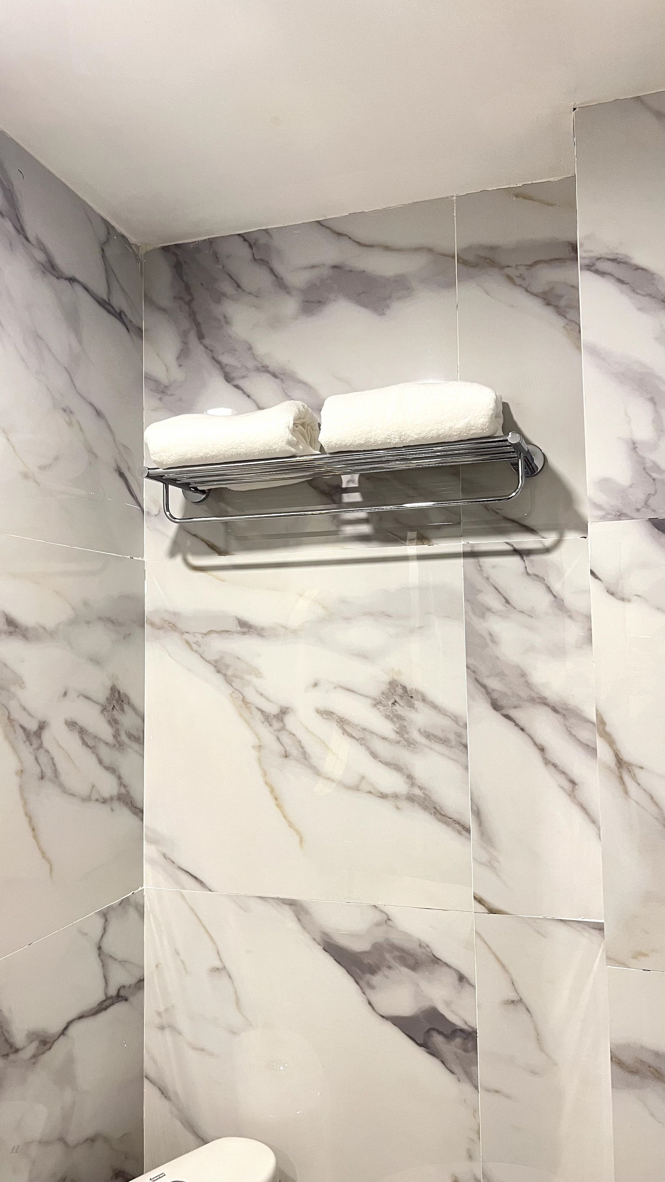 Baño con pared de mármol y toallero con dos toallas.