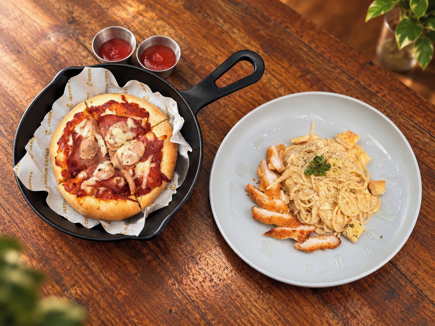 Une pizza garnie et une assiette de pâtes au poulet, le tout posé sur une table en bois.