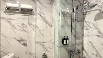A bathroom with a glass-enclosed shower, a towel rack with two towels, and two bottles of shampoo on a shelf.