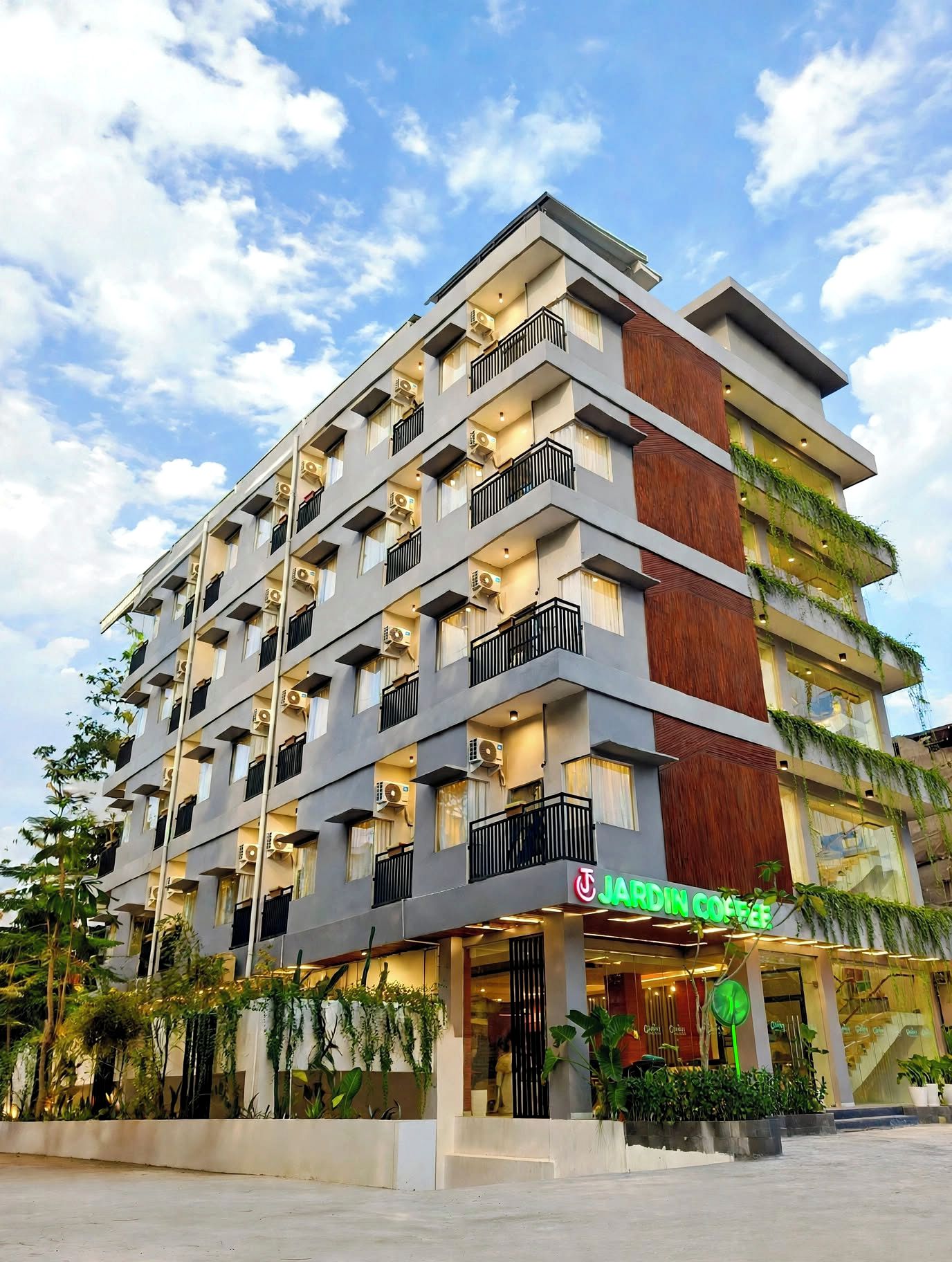Un hôtel à plusieurs étages, doté de balcons, de climatiseurs et d’une devanture avec une enseigne verte.
