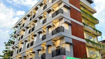 Un hôtel à plusieurs étages, doté de balcons, de climatiseurs et d’une devanture avec une enseigne verte.