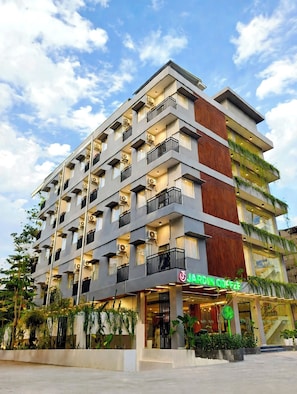 A multi-story hotel with balconies, air conditioning units, and a storefront with a green sign. - Qafotel Boutique (Balikpapan)