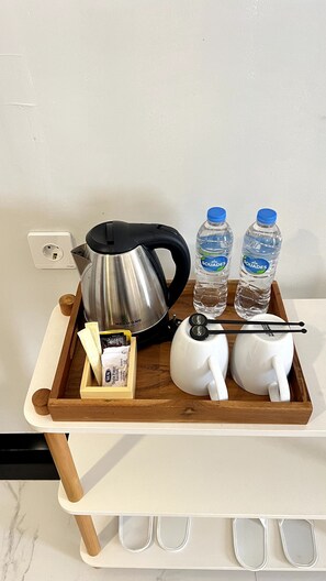 A tray with a kettle, two water bottles, a teapot, and sachets on a white countertop. - Qafotel Boutique (Balikpapan)