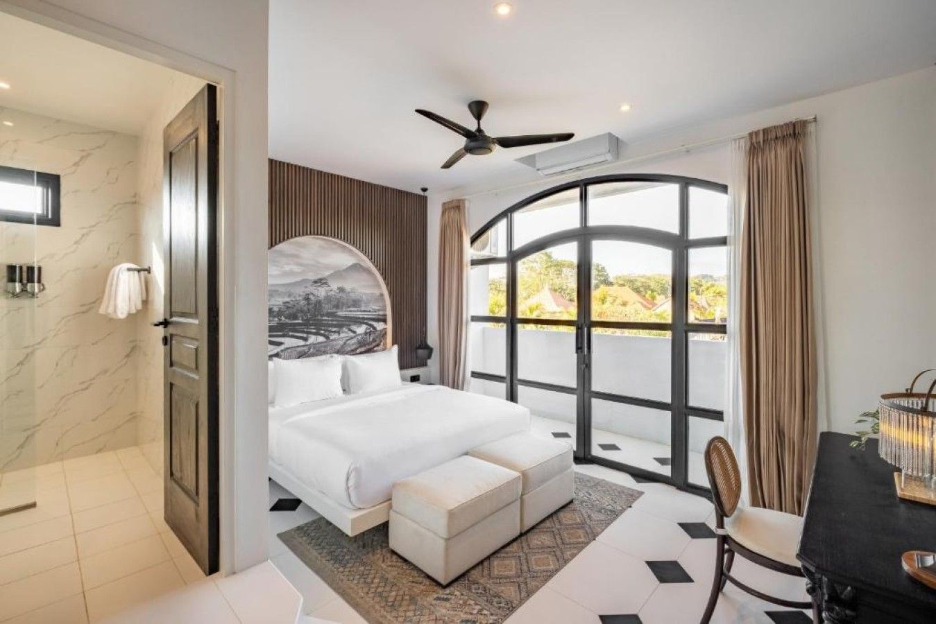 A bedroom with a bed, a desk, a chair, a large window, and a ceiling fan.