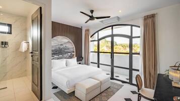 A bedroom with a bed, a desk, a chair, a large window, and a ceiling fan.