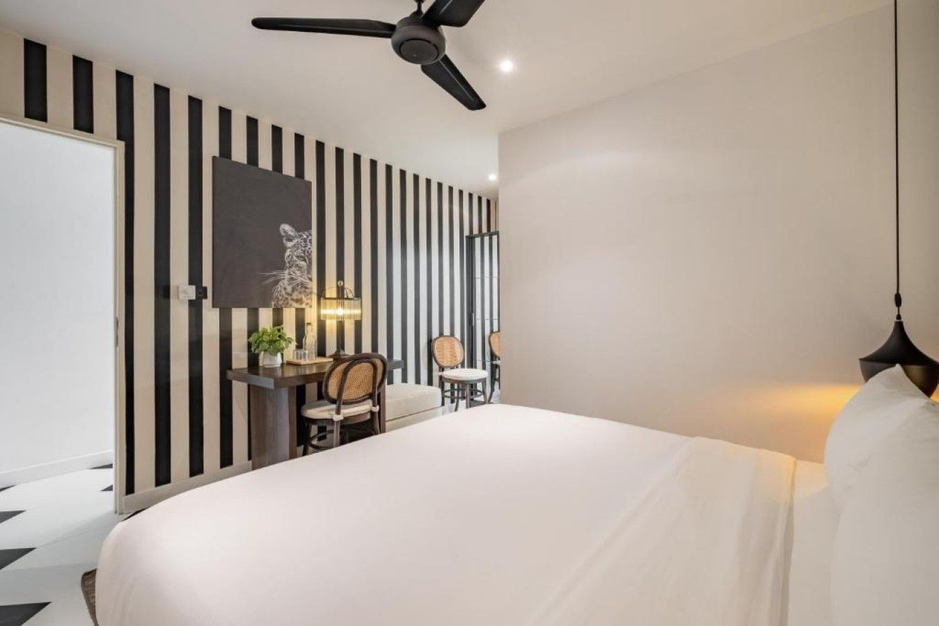 Une chambre d’hôtel avec un grand lit, un bureau avec des chaises, un ventilateur de plafond et un mur à rayures verticales.