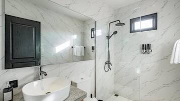 Une salle de bain moderne avec un grand lavabo blanc, un meuble en bois foncé, une cabine de douche en verre et des murs en marbre.