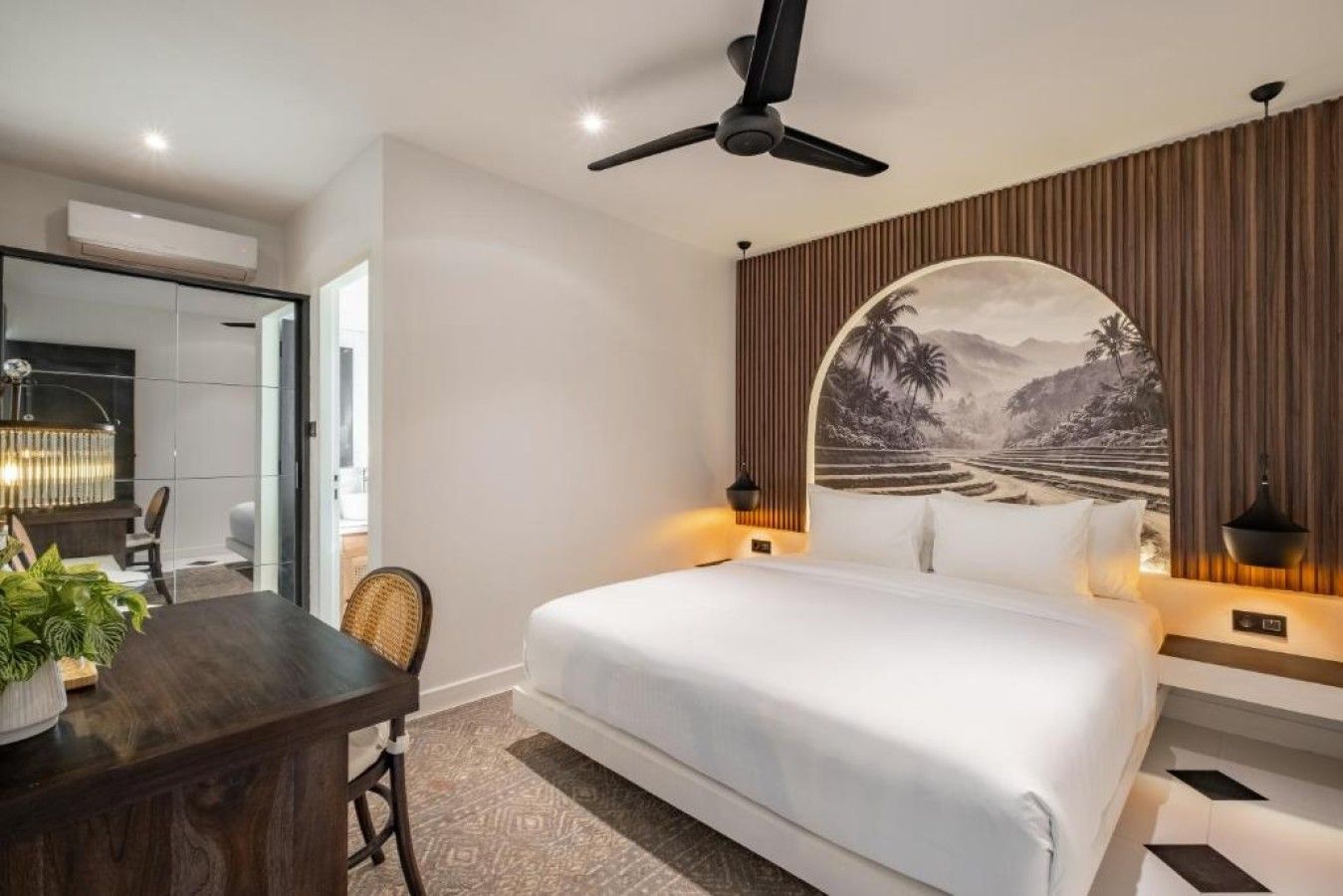 Ein modernes Hotelzimmer mit einem großen Bett, einem Schreibtisch und Blick auf eine tropische Landschaft.