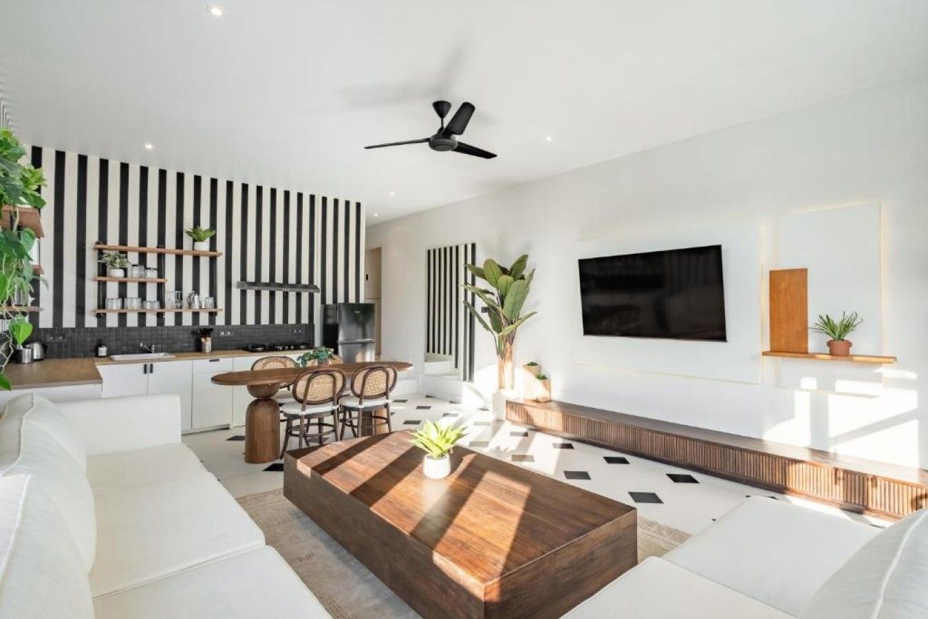 Un salon moderne comprenant un coin repas, un téléviseur à écran plat fixé au mur et un ventilateur de plafond.
