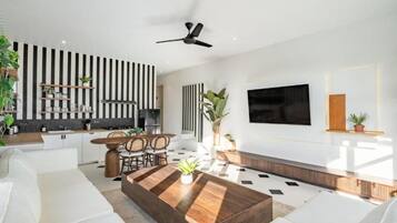 Un salon moderne comprenant un coin repas, un téléviseur à écran plat fixé au mur et un ventilateur de plafond.