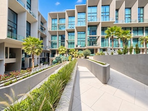 A modern hotel with a central courtyard, multiple balconies, and lush landscaping. - Cozy Studio with Pool & Gym Near Circle Mall (Dubai)