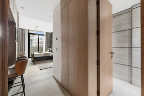 Et moderne hotelværelse med seng, siddeområde med stole og udsigt over byen gennem store vinduer.