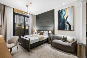 A modern hotel room with a bed, a sofa, a chair, a desk, and a large window. - Cozy Studio with Pool & Gym Near Circle Mall (Dubai)