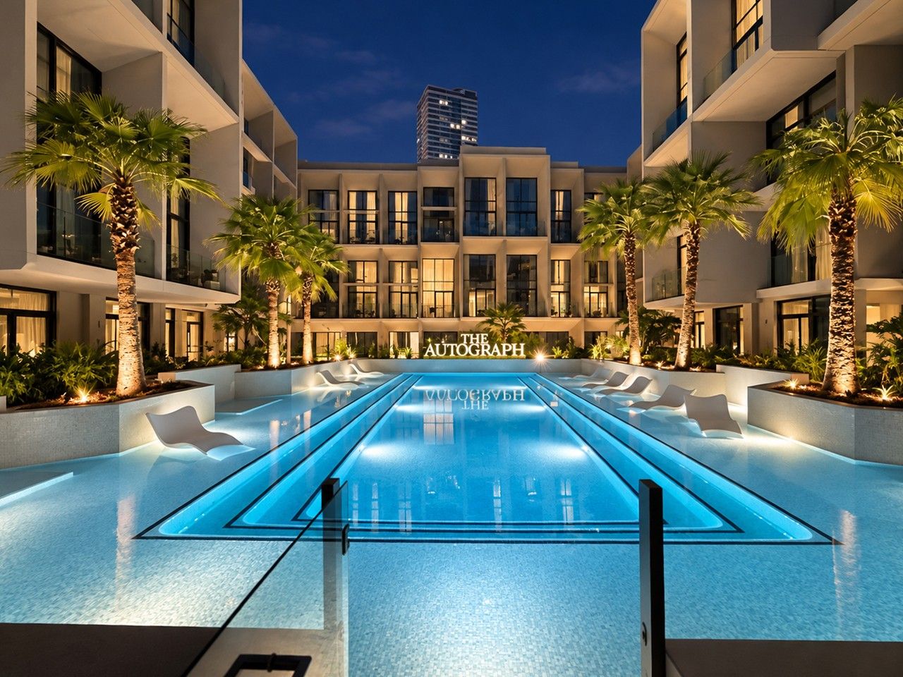 A swimming pool with lounge chairs and palm trees, surrounded by modern buildings with balconies.