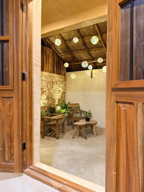 An open wooden door leading to a room with a stone wall, wooden furniture, and a thatched ceiling with hanging lights. - Las JULIAS Cuarto privado (Mérida)