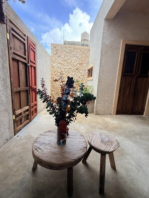 A courtyard with a stone wall, a wooden door, and a potted plant on a round wooden table. - Las JULIAS Cuarto privado (Mérida)