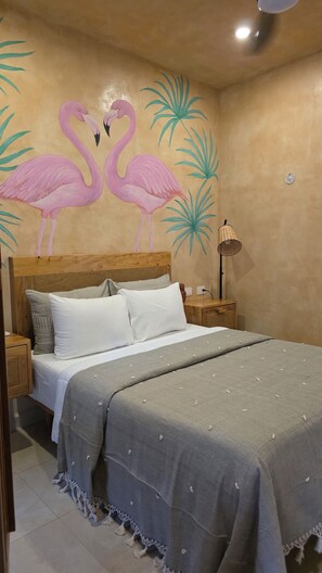 A bedroom with a bed, nightstands, a lamp, and a wall mural of flamingos. - Las JULIAS Cuarto privado (Mérida)