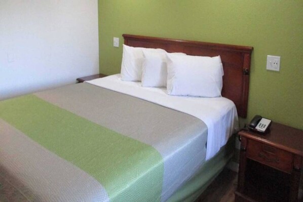 A single bed with a wooden headboard, a green and white bedspread, and a bedside table with a telephone. - 1 King Bed | Non-Smoking, Micfridge (Fresno CA)