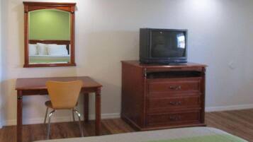 A room with a wooden desk, a chair, a television on a wooden cabinet, and a mirror on the wall.