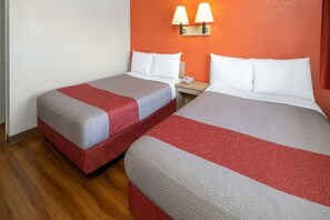 A hotel room with two beds, each with a red and grey bedspread, and a nightstand with a lamp between them.