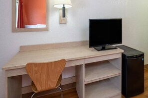 A room with a wooden desk, a black monitor, a chair, and a small black refrigerator.