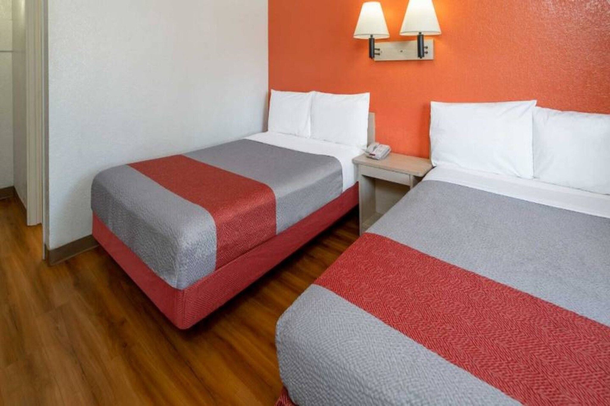 Ein Hotelzimmer mit zwei Betten, jeweils mit einer roten und grauen Decke, einem Nachttisch mit Telefon und einer Wandlampe.