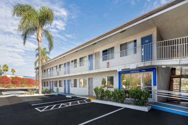 A motel with a two-story structure, a parking lot, and a palm tree.