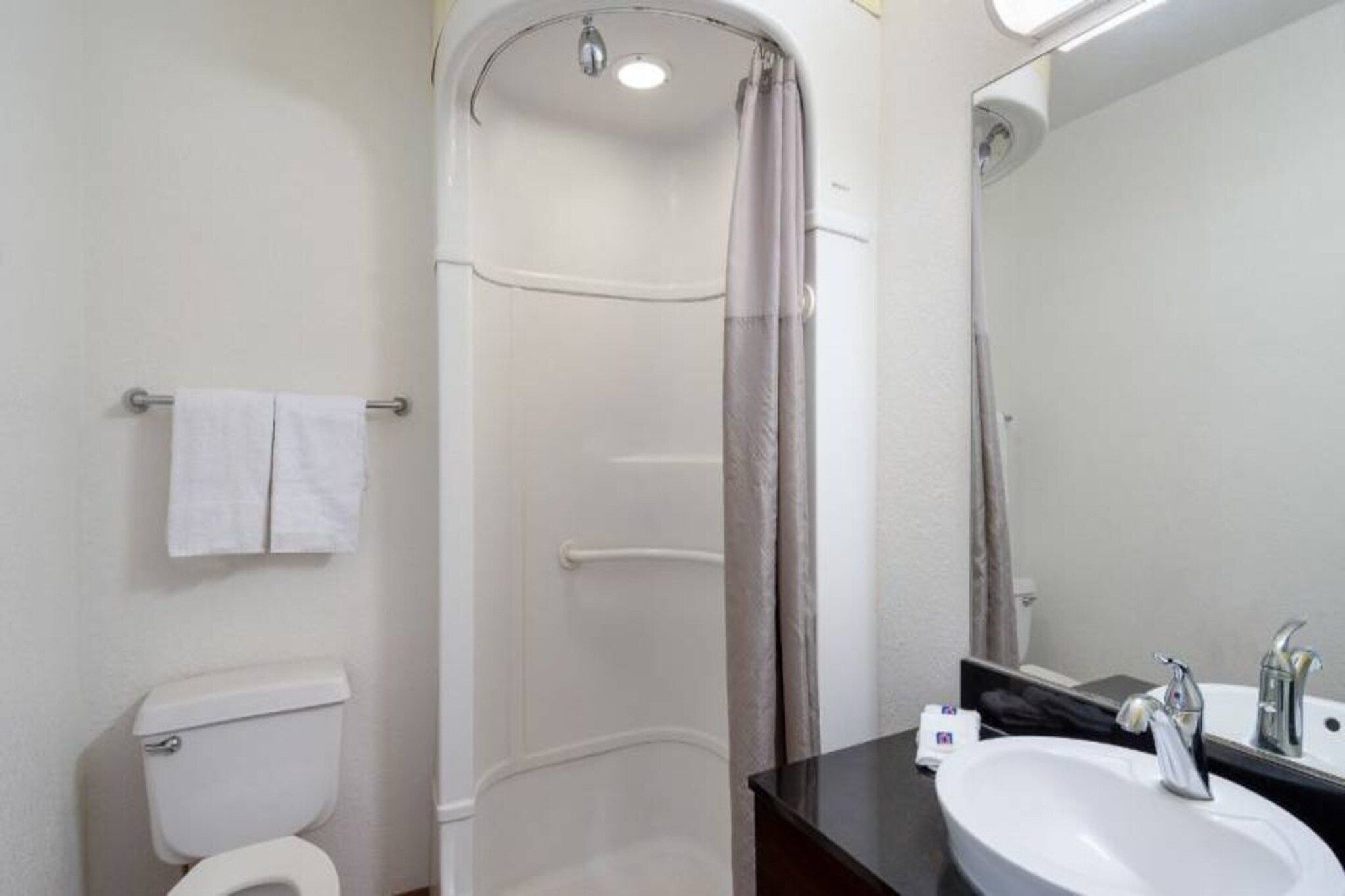 Ein Badezimmer mit Toilette, einer Dusche mit Vorhang, einem Waschbecken mit Spiegel und einem Handtuchhalter.