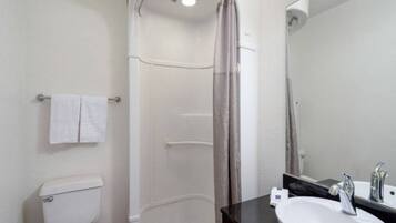 Ein Badezimmer mit Toilette, einer Dusche mit Vorhang, einem Waschbecken mit Spiegel und einem Handtuchhalter.