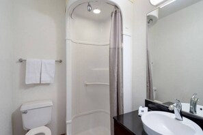 A bathroom with a toilet, a shower with a curtain, a sink with a mirror, and a towel rack.