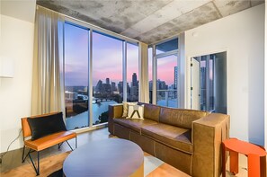 A modern living room with a large window offering a city view, a brown leather sofa, a wooden coffee table, and a red side table. - Rooftop Pool + Skyline Views • Near Rainey Street + Downtown | Panoramic Summit (Austin)