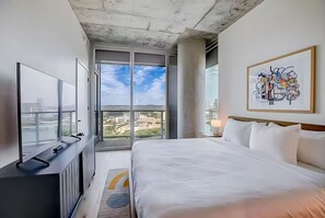 A modern hotel room with a large bed, a flat-screen TV, and a city view through large windows. - Rooftop Pool + Skyline Views • Near Rainey Street + Downtown | Panoramic Summit (Austin)