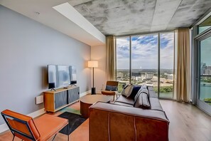 A modern living room with a flat-screen TV, a sofa, a coffee table, and a lamp. - Rooftop Pool + Skyline Views • Near Rainey Street + Downtown | Panoramic Summit (Austin)