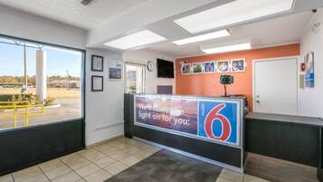 A hotel reception area with a large sign displaying the number 6, a reception desk, a clock, and framed pictures on the wall.