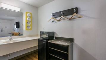 A compact hotel room with a kitchenette, a mirror, a small TV, and a coat rack.