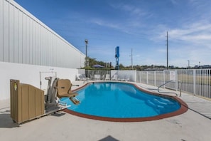 A swimming pool with a white fence, lounge chairs, and a portable toilet.