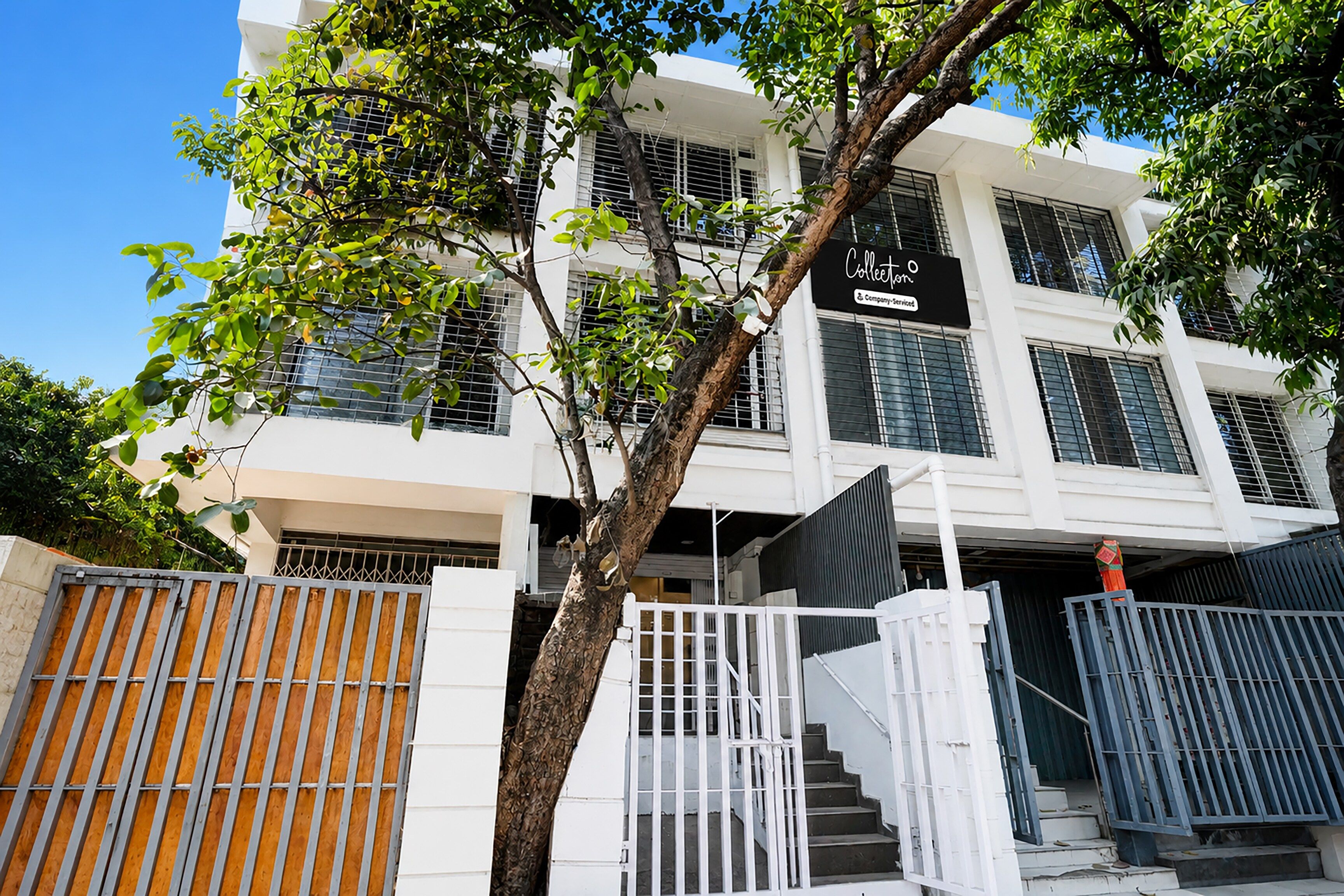 A multi-story building with a gated entrance, a staircase, and a tree in front.