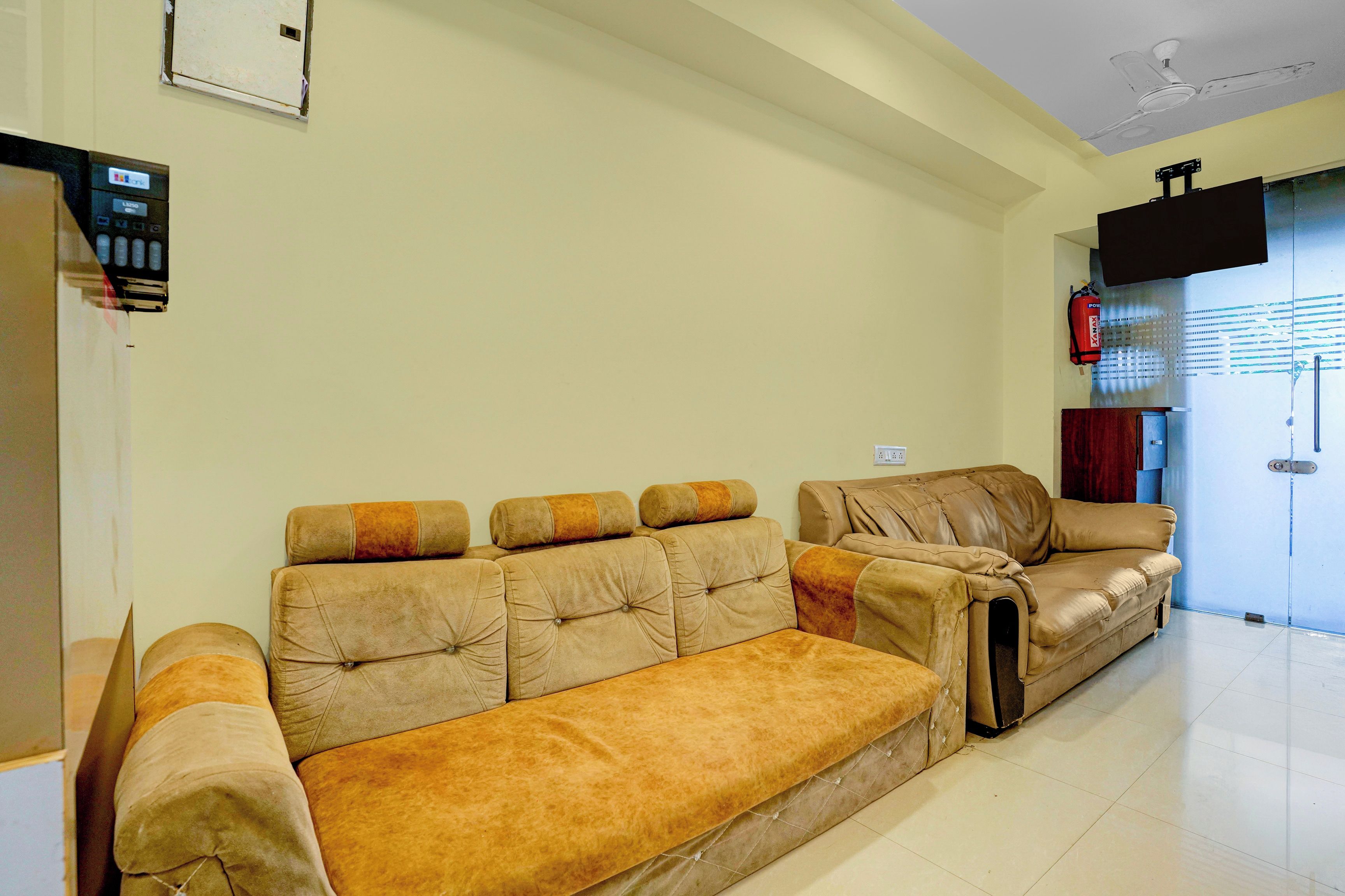 A living room with a sofa set, a television mounted on the wall, and a fire extinguisher.