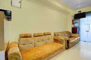 A living room with a sofa set, a television mounted on the wall, and a fire extinguisher. - Collection O Santacruz Railway Station (Mumbai)
