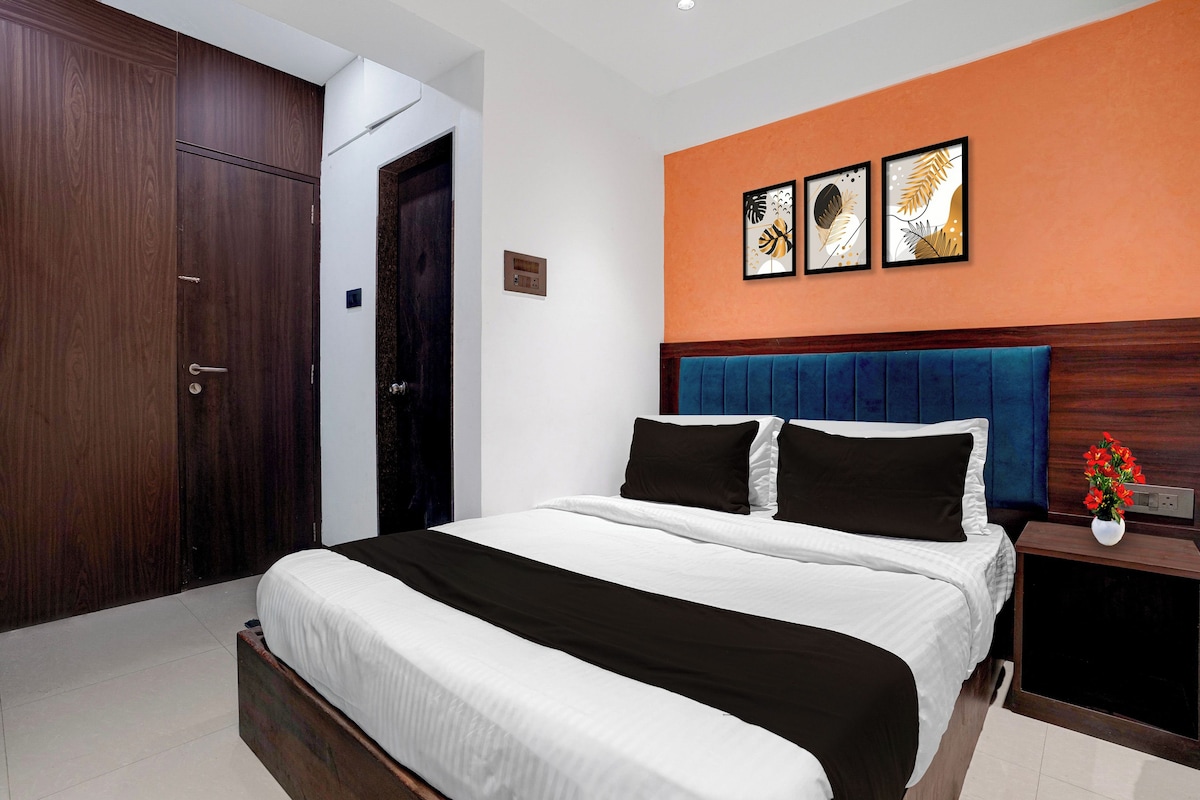 A hotel room with a large bed, a nightstand, a wall-mounted power outlet, and a door.